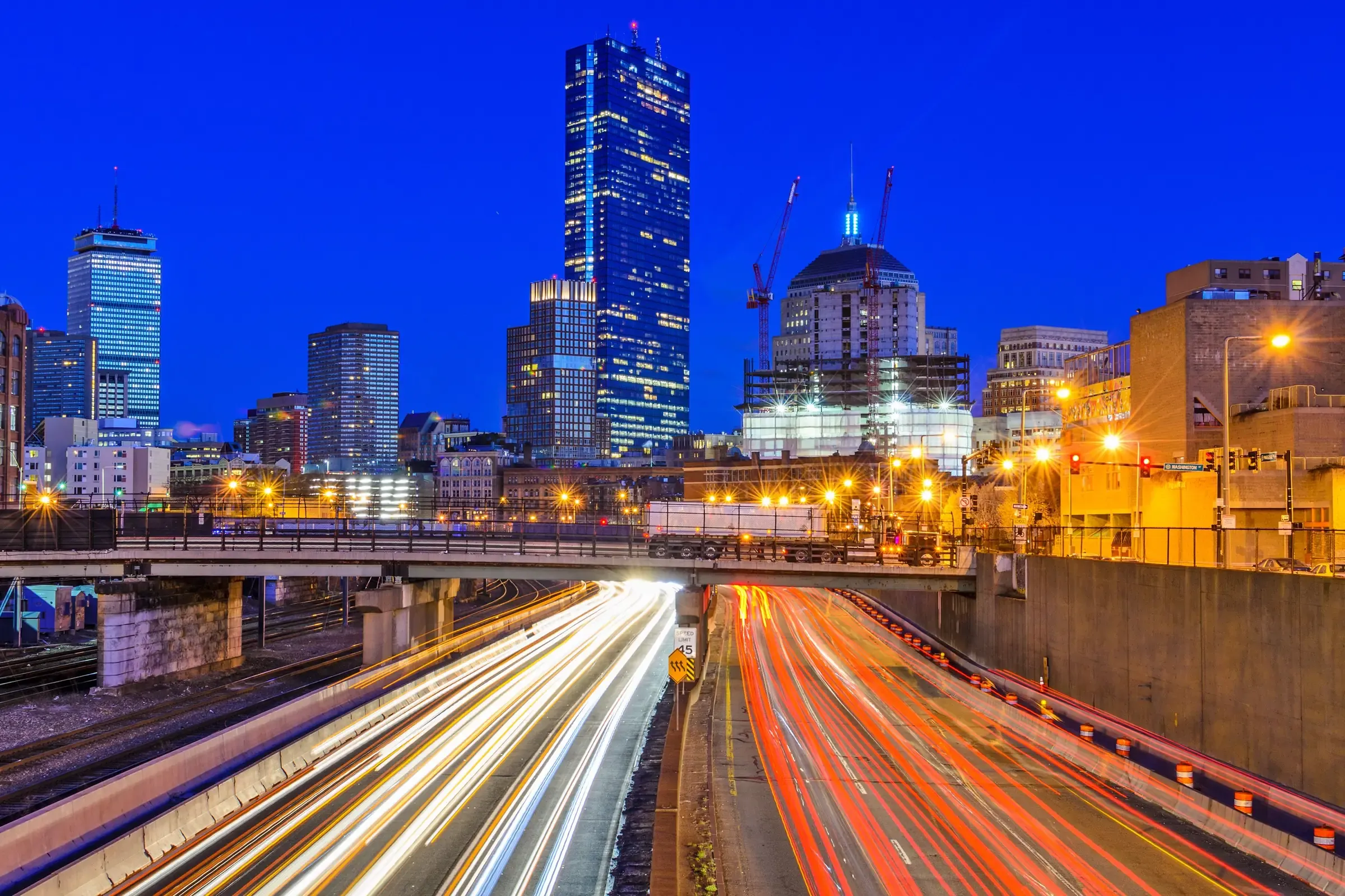 The Boston skyline at dusk above streaks of traffic light