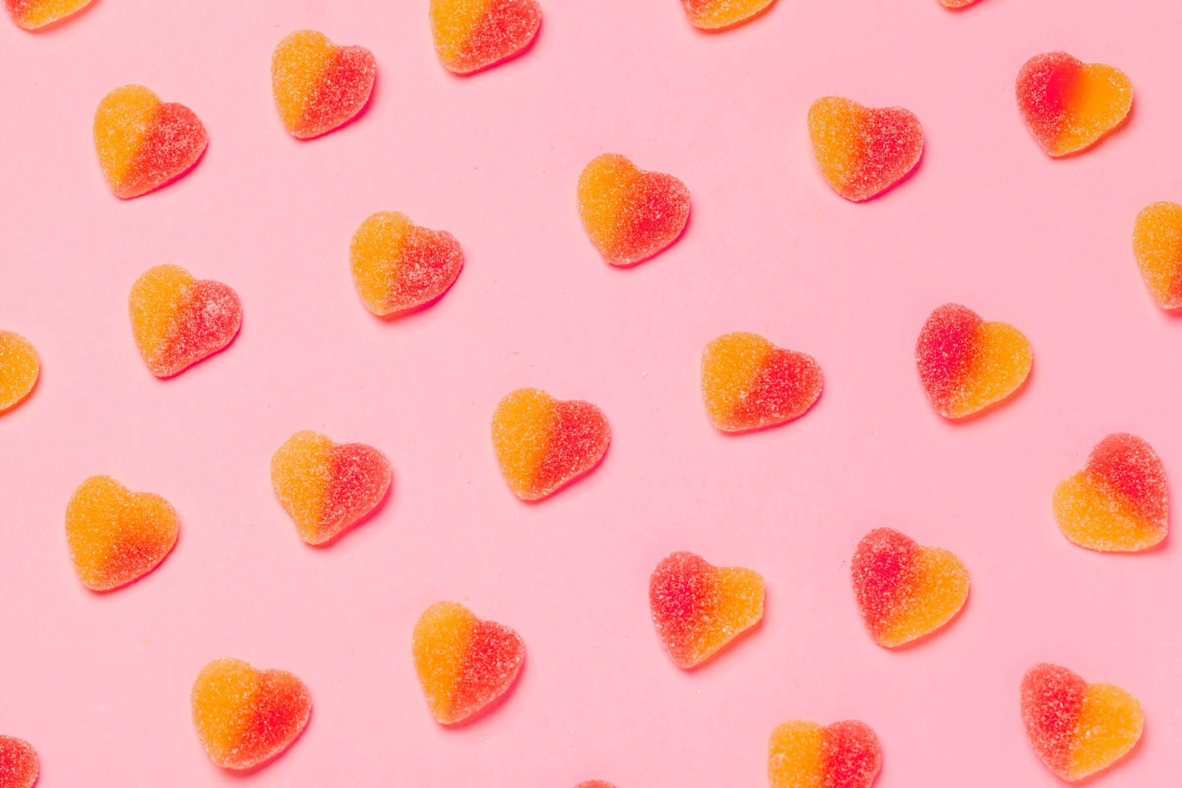 Sugar-dusted heart-shaped jelly lollies on a pink background